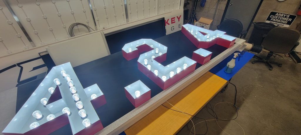 Red and white aluminum 424 numerals with LED bulbs on the bench during fabrication