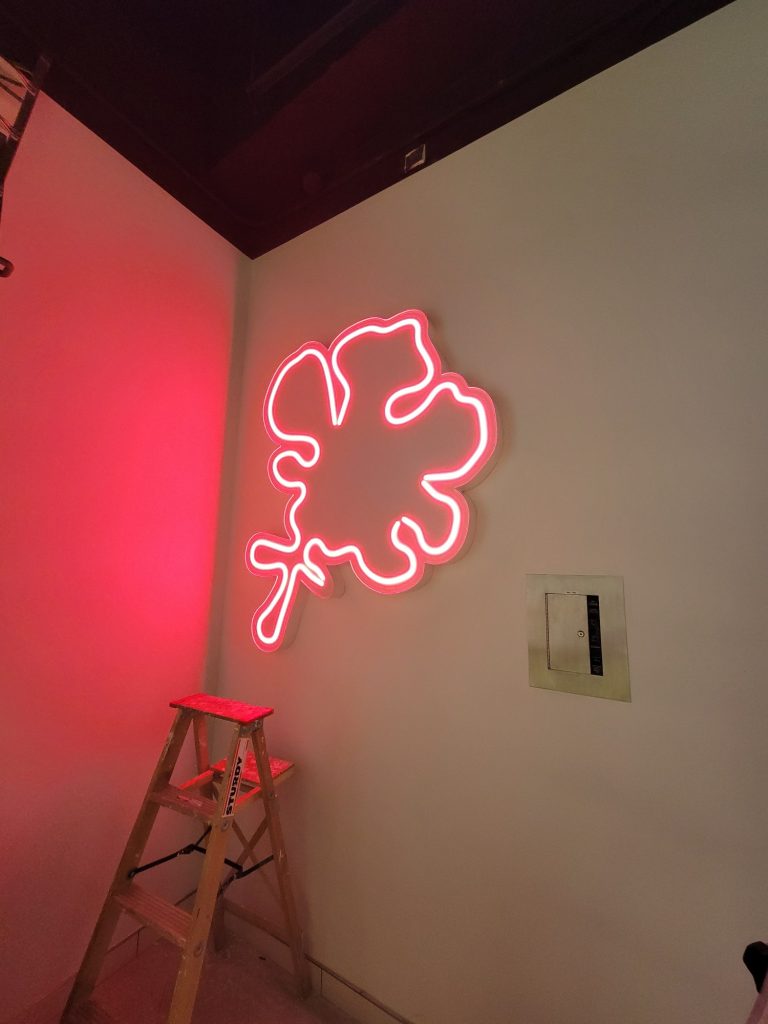 Pink LED neon-flex flower logo glowing on an interior wall
